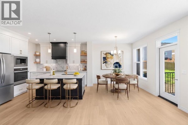 Spacious kitchen with white cabinetry, a dark island with bar stools, and a dining area. - 63 Annette Rise Nw, Calgary