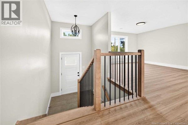 Interior view of the main floor with light wood floors, white door, and staircase. - 63 Ardoise Street, Moncton