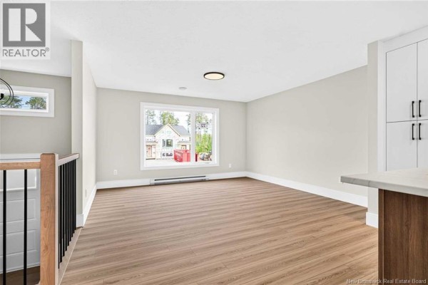 Living area with light wood floors, large window overlooking the street, and white cabinets. - 63 Ardoise Street, Moncton