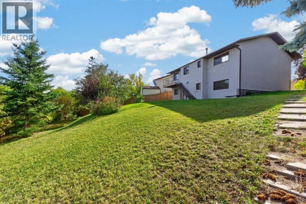 View of the side and backyard of a house, with a sloped grassy lawn and mature trees. - 63 Beaconsfield Crescent Nw, Calgary