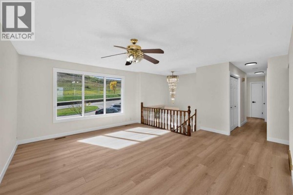 Bright living room with a large window, light wood flooring, a chandelier, and a ceiling fan. - 63 Beaconsfield Crescent Nw, Calgary