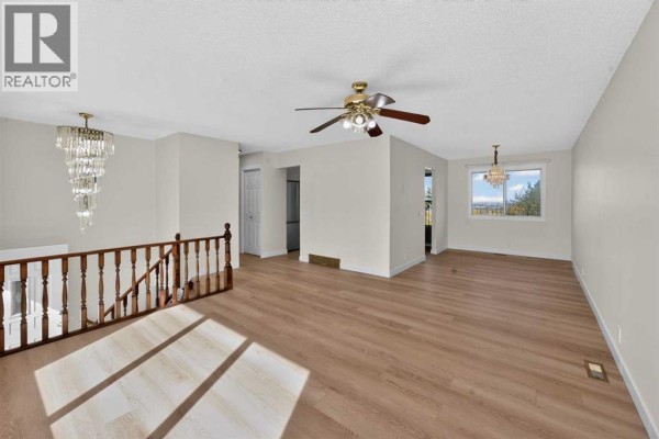 Spacious living area with light grey walls, light wood floors, two chandeliers, and a view of the city. - 63 Beaconsfield Crescent Nw, Calgary