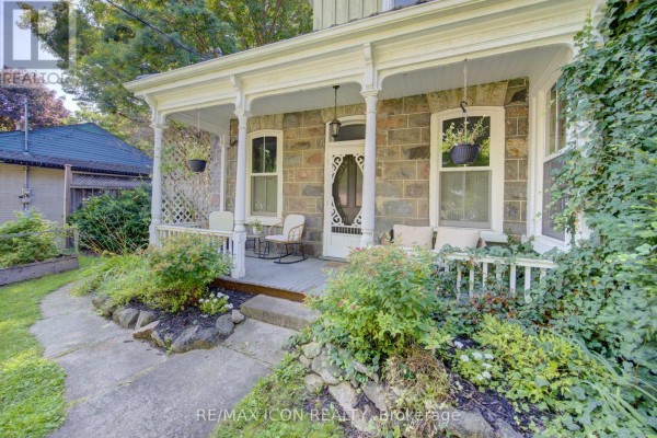 Close-up of the stone house porch with decorative pillars, rocking chairs, and hanging plants. - 63 Birch Street, Cambridge