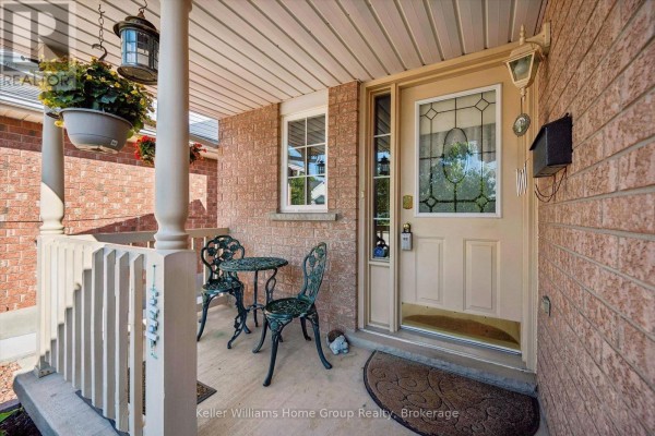 Front porch with two green metal chairs, a small table, and a decorative hanging planter. - 63 Boulder Crescent, Guelph