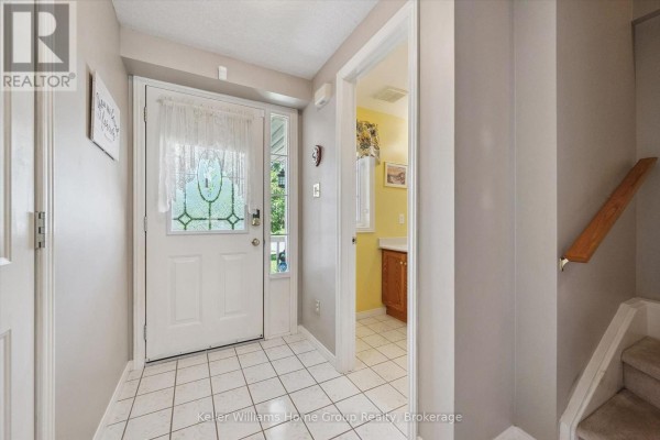 Interior view of a house entryway with white tiled floor, white front door, and a hallway leading to a bathroom. - 63 Boulder Crescent, Guelph