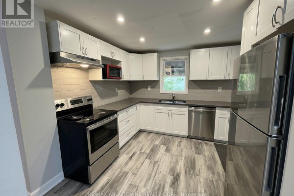 L-shaped kitchen with white cabinets, stainless steel appliances, and grey tile backsplash. - 63 Gage Avenue N, Hamilton