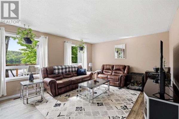 Living room with two brown leather sofas, a patterned rug, a coffee table, and large windows overlooking the lake. - 63 Heyden Lake Rd, Aweres