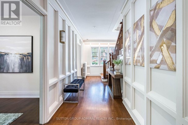 Long hallway with paneled walls, hardwood floors, bench, and abstract art. - 63 Highland Avenue, Toronto