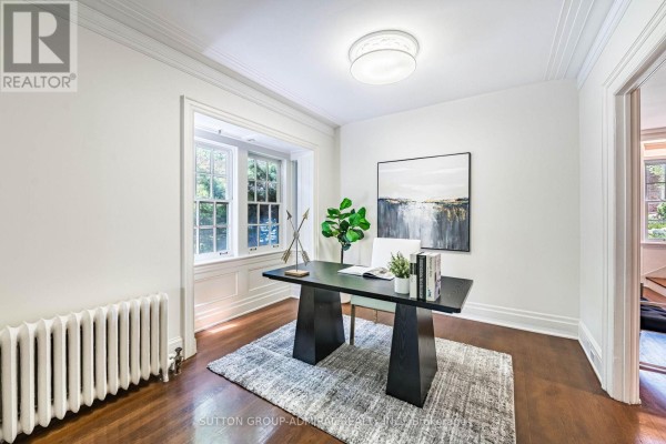 Home office with dark wood desk, white chair, rug, and large window. - 63 Highland Avenue, Toronto