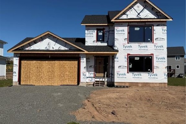 Exterior front view of a house under construction, covered in white Tyvek wrap, with a wooden garage door. - 63 Melbourne Crescent, Moncton