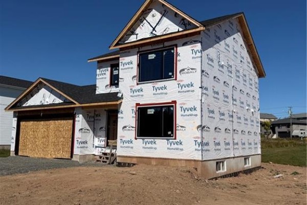 Side view of a house under construction, covered in white Tyvek wrap, with dark-framed windows installed. - 63 Melbourne Crescent, Moncton