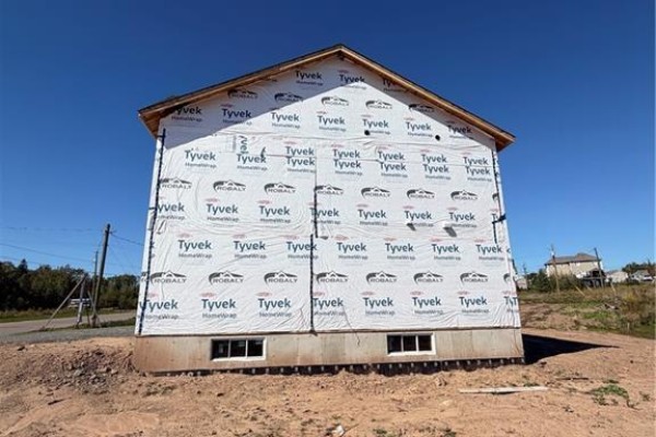 Rear exterior of a house under construction, covered in white Tyvek wrap, showing foundation windows. - 63 Melbourne Crescent, Moncton
