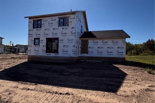 Side and rear exterior view of a house under construction, covered in Tyvek wrap, on a dirt lot. - 63 Melbourne Crescent, Moncton