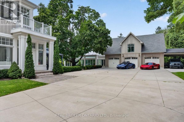 View of the rear of the house with a large driveway, three garage doors, and two sports cars. - 63 Mill Street S, Hamilton