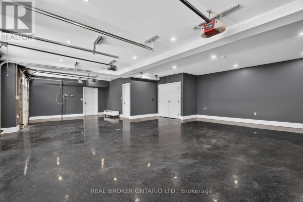 Interior of a spacious, empty garage with dark gray walls, a glossy speckled floor, and four garage doors. - 63 Mill Street S, Hamilton