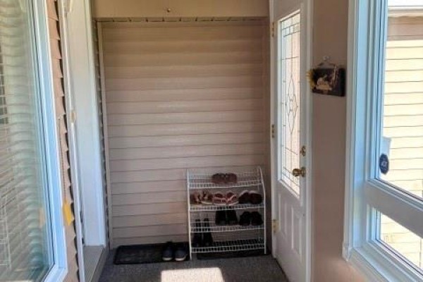 Covered entryway with a white door, shoe rack, and beige siding. - 63 Parise Street, Caraquet