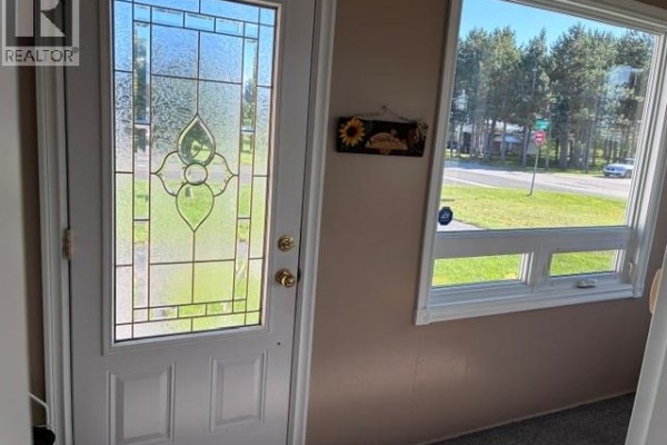 Front door with decorative glass panels, a metal rack with shoes, and a window. - 63 Parise Street, Caraquet