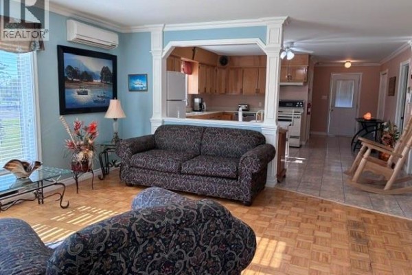 Living room with patterned sofas, a glass coffee table, and view of the kitchen. - 63 Parise Street, Caraquet