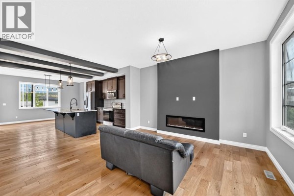 Open concept living area with a gray fireplace feature wall, leather sofa, and hardwood floors. - 63 Precedence Link, Cochrane