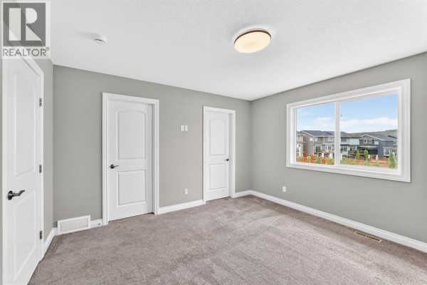 Empty bedroom with gray walls, carpet, two white doors, and a window with neighborhood view. - 63 Precedence Link, Cochrane
