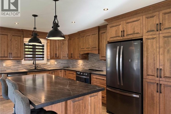 Kitchen with wood cabinets, granite countertops, stainless steel appliances, and a large island. - 63 Premiere Avenue, Sainte Anne De Madawaska