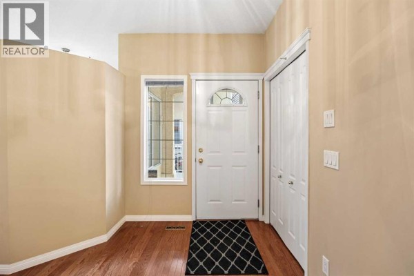 Interior hallway with hardwood floors, white baseboards, and double doors leading to closets. - 63 Scimitar Heath Nw, Calgary