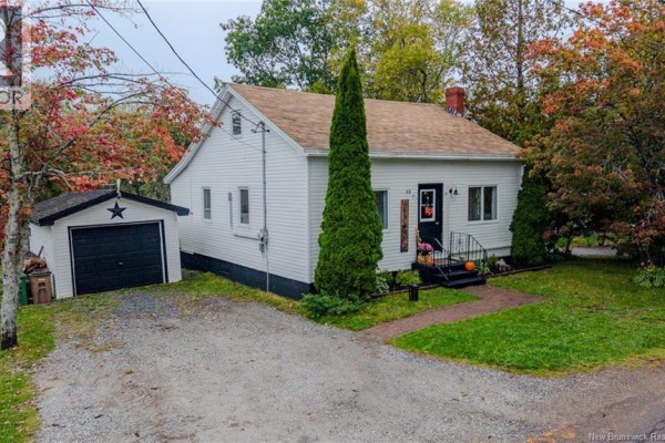 Side and front view of a white, single-story house with a detached garage and a tall evergreen tree. - 63 Stevens Road, Saint John