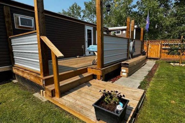 Wooden deck with corrugated metal railings and steps attached to a brown mobile home. - 63 Westwood Court, Innisfail