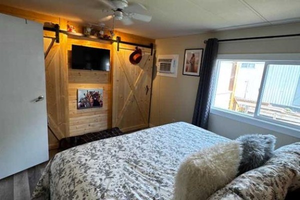 Bedroom with a queen bed, barn doors, mounted television, and a window. - 63 Westwood Court, Innisfail