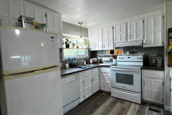White L-shaped kitchen with a refrigerator, dishwasher, stove, and cabinetry. - 63 Westwood Court, Innisfail