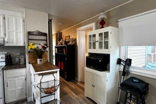 Kitchenette area with white cabinets, a microwave, a baker's rack, and a butcher block island. - 63 Westwood Court, Innisfail