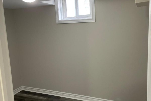 Empty room with light grey walls and dark laminate flooring, featuring a single window. - 630 Cartier Avenue, Oshawa