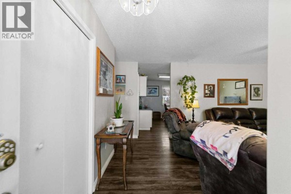 Interior hallway with wooden flooring, plants, and a table leading to living areas. - 6304 39 Avenue, Camrose