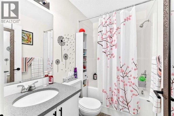 Bathroom with a vanity, toilet, bathtub with shower, and a floral-patterned shower curtain. - 6305, 151 Legacy Main Street Se, Calgary