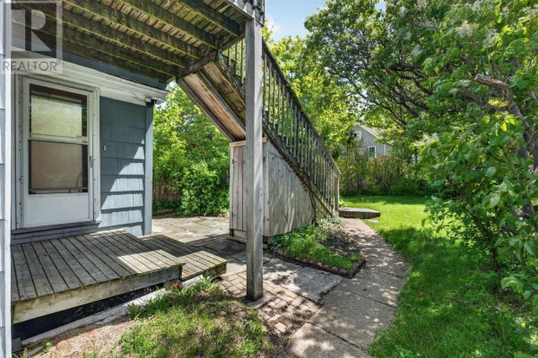 Side view of a house with a wooden deck, stairs, and a paved pathway leading to a grassy area. - 6308 Bayers Road, Halifax