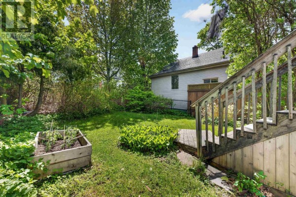Backyard with a wooden planter box, green grass, mature trees, and a portion of the house visible. - 6308 Bayers Road, Halifax