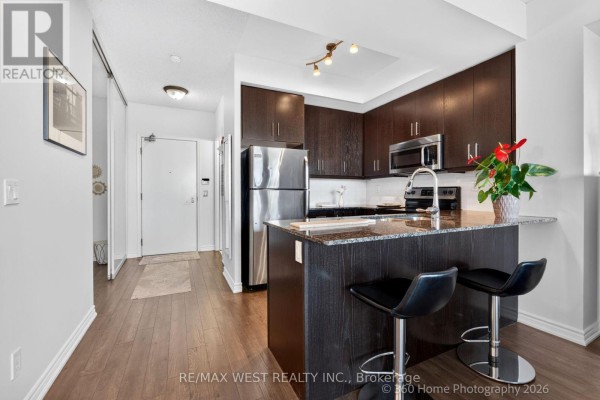 Open-concept kitchen with dark wood cabinets, granite island, stainless steel appliances, and two bar stools. - 631 - 15 James Findlay Way, Toronto