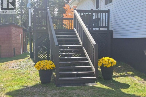 Dark wooden deck stairs with lattice detailing, flanked by large planters of yellow flowers. - 631 Gloucester Junction Road, Gloucester Junction