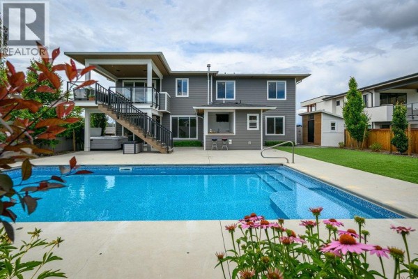 Exterior view of a modern house with a manicured lawn, purple flowers, and a driveway with two garage doors. - 631 Mt Ida Crescent, Coldstream