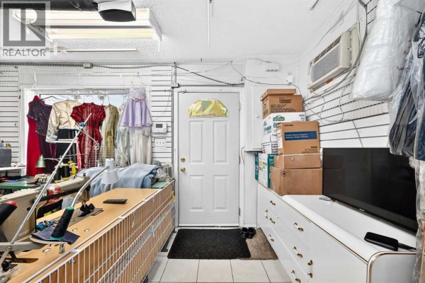 Interior view of a workshop with sewing machines, fabric, and finished garments on display, with a door in the background. - 632 Marsh Road Ne, Calgary