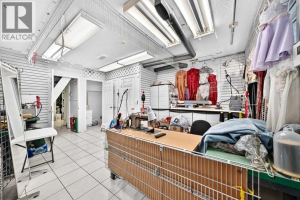 Wide interior shot of the workshop, showing sewing stations, garment racks, mirrors, and a staircase leading to another level. - 632 Marsh Road Ne, Calgary