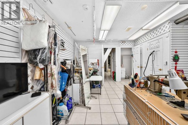 View of the workshop interior from the side, displaying clothing racks, sewing equipment, a mirror, and doorways. - 632 Marsh Road Ne, Calgary