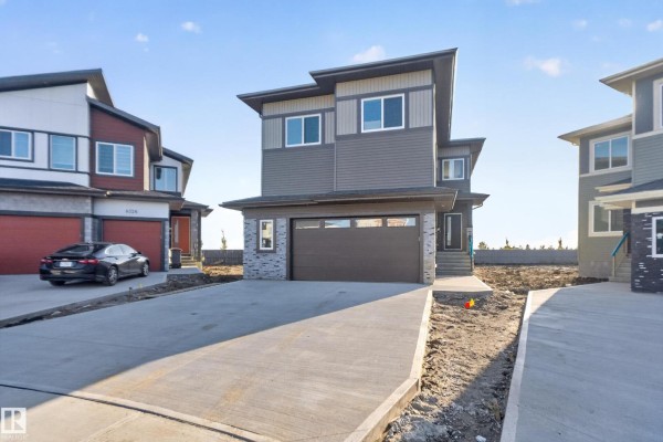 Modern townhouse exterior with grey siding, red garage door, and daytime sky. - 6320 24 St Ne Ne, Rural Leduc County