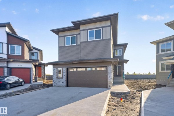 Front exterior of a modern townhouse with grey siding and a double garage door. - 6320 24 St Ne Ne, Rural Leduc County