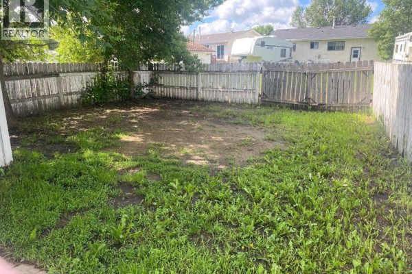 Backyard with a wooden fence, grass, and dirt patch. - 6321-b Enevold Drive, Camrose
