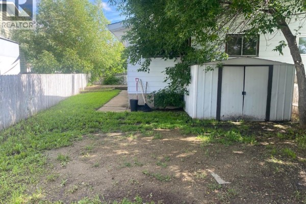 Side view of the backyard with a shed, grass, and a wooden fence. - 6321-b Enevold Drive, Camrose