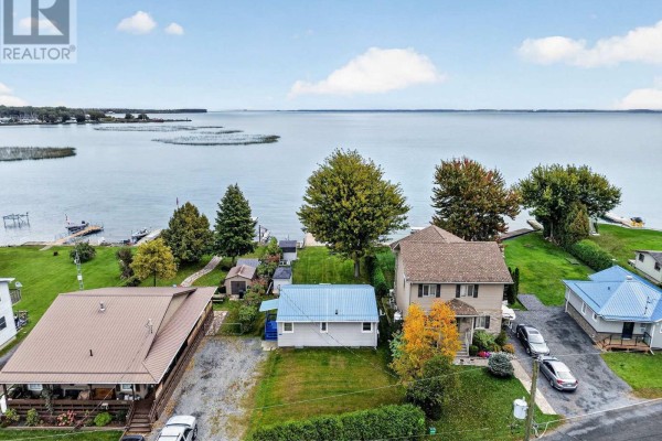Aerial view of waterfront properties, including a grey cottage, with a wide blue lake in the background. - 6325 78th Avenue, South Glengarry