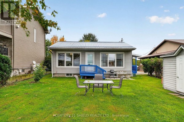 Rear exterior of a grey cottage with a blue deck and a simple metal table and chairs on the lawn. - 6325 78th Avenue, South Glengarry