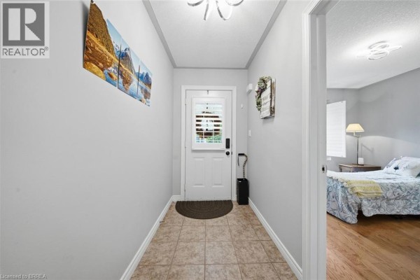 Interior view of a narrow hallway with tiled floor, light grey walls, and artwork. - 633 Park Road N Unit# 8, Brantford