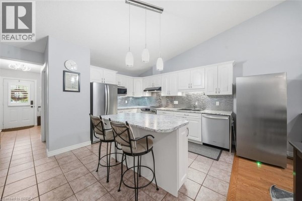 Spacious white kitchen with granite island, stainless steel appliances, and vaulted ceiling. - 633 Park Road N Unit# 8, Brantford